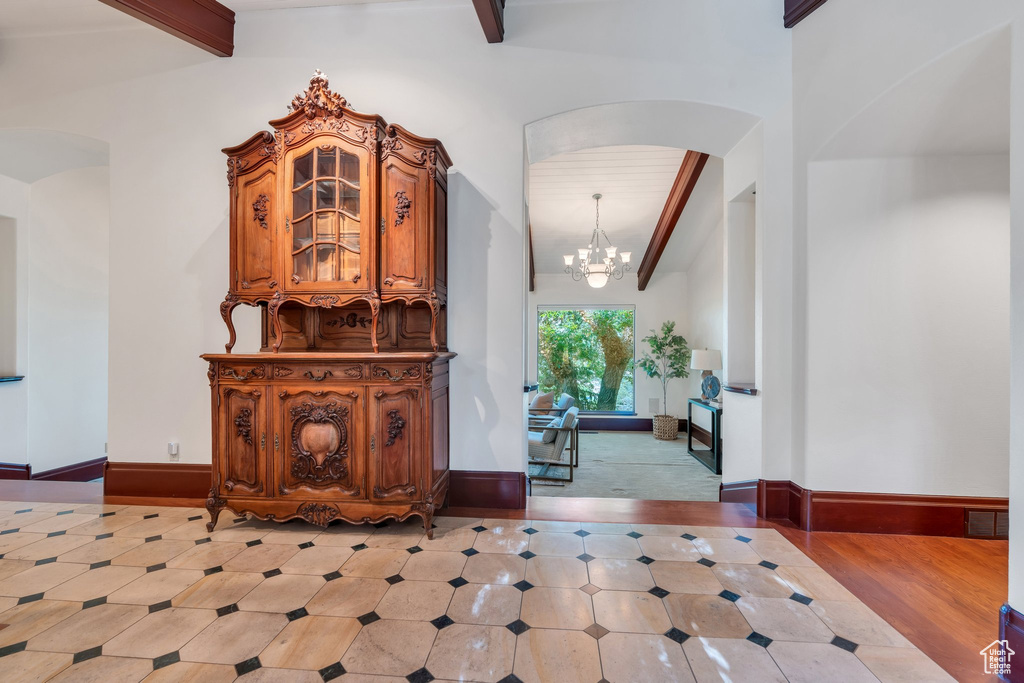 Hall featuring beam ceiling, a chandelier, arched walkways, and baseboards