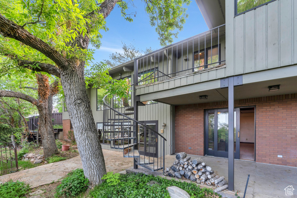 View of side of property with brick siding, stairway, a patio area, a balcony, and board and batten siding