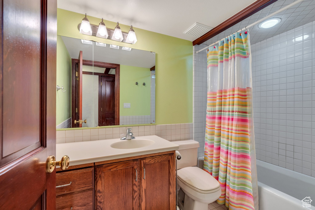 Full bath with tile walls, shower / tub combo with curtain, toilet, and vanity