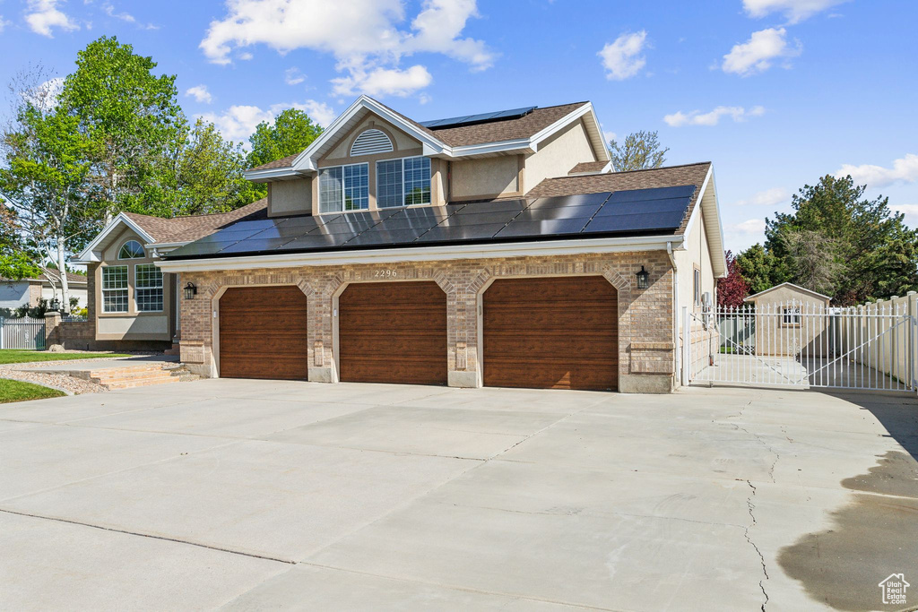 View of front facade with solar panels, concrete driveway, and roof with shingles