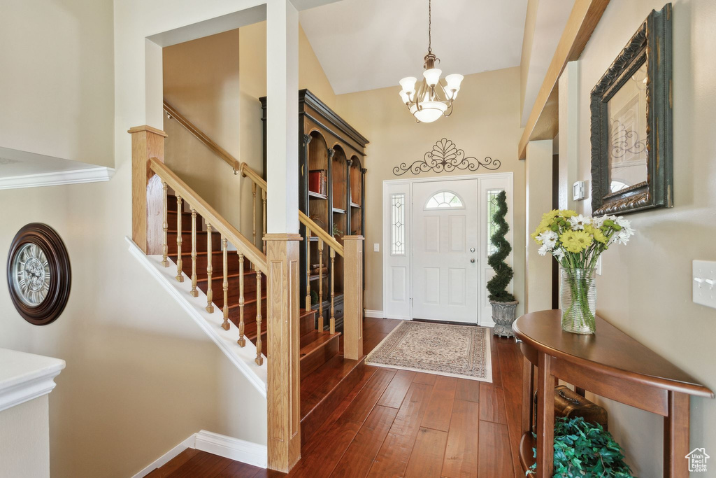 Foyer entrance with stairs, a chandelier, baseboards, dark wood-style floors, and a towering ceiling