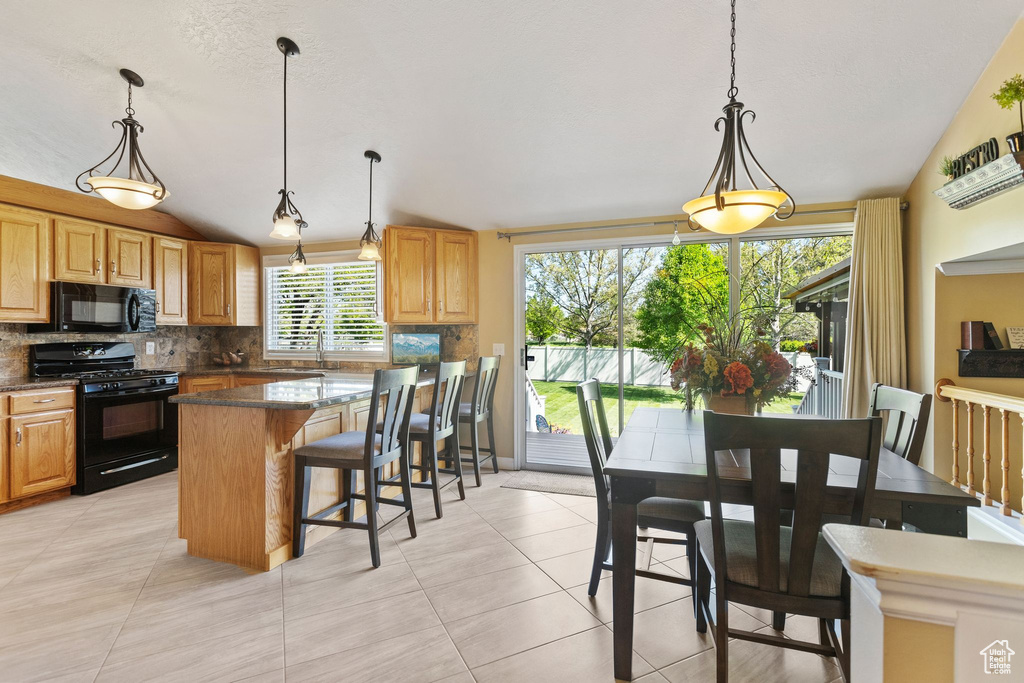 Kitchen with black appliances, a sink, backsplash, a breakfast bar area, and hanging light fixtures