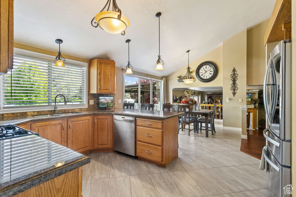 Kitchen with stainless steel appliances, a sink, brown cabinets, hanging light fixtures, and vaulted ceiling