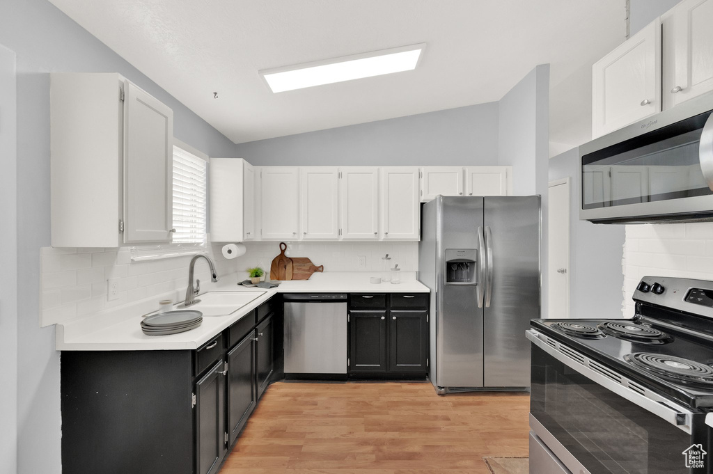 Kitchen with appliances with stainless steel finishes, a sink, lofted ceiling, white cabinets, and light wood-type flooring