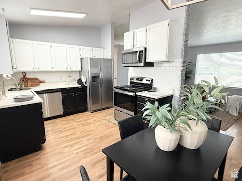Kitchen featuring appliances with stainless steel finishes, white cabinetry, light countertops, light wood-style floors, and a sink