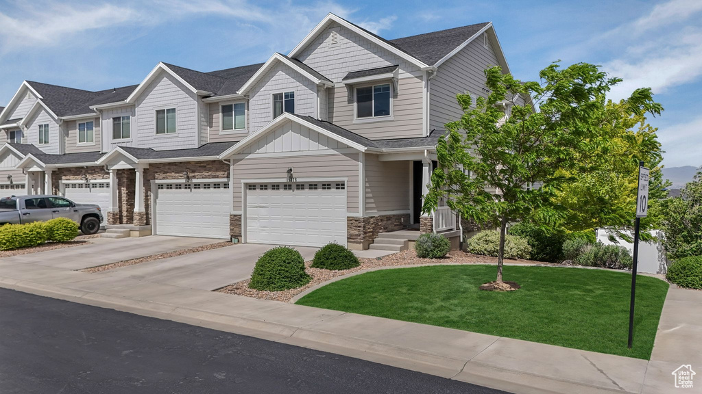 Multi unit property with a garage, driveway, a front lawn, stone siding, and board and batten siding