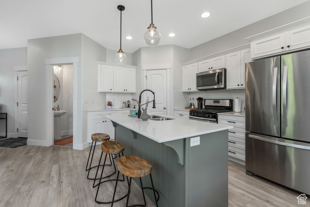 Kitchen featuring stainless steel appliances, a sink, decorative backsplash, a kitchen breakfast bar, and light wood-style flooring