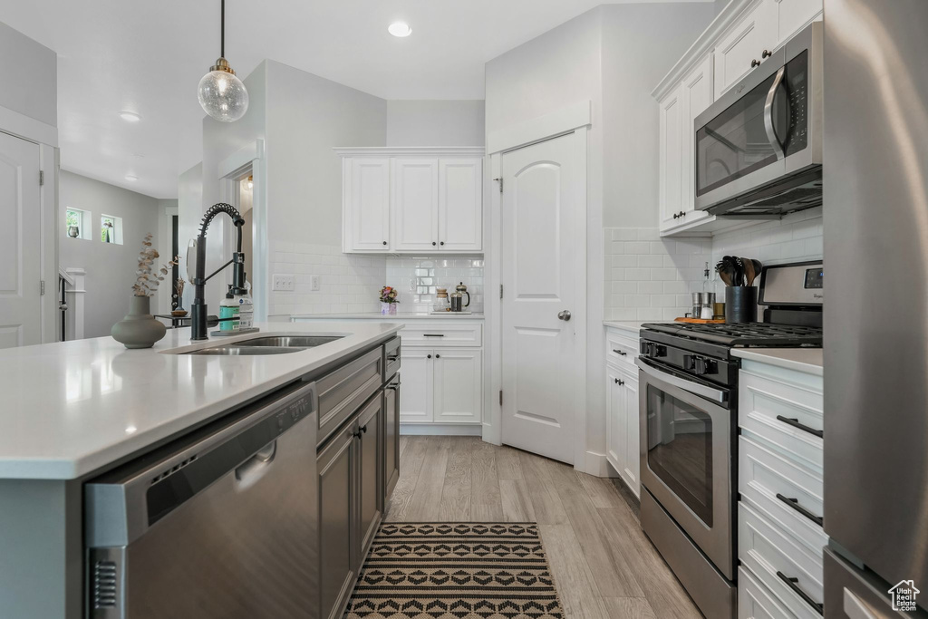 Kitchen with stainless steel appliances, a sink, light countertops, light wood-style flooring, and white cabinetry