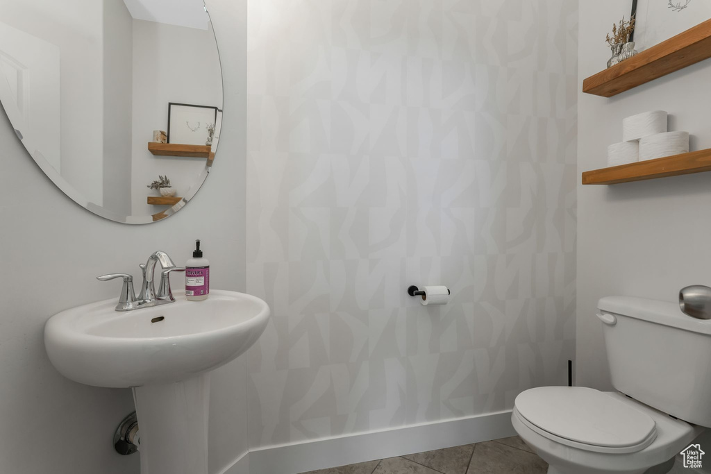 Bathroom with toilet, baseboards, tile patterned floors, and a sink