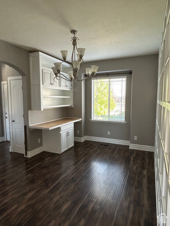 Unfurnished dining area with arched walkways, baseboards, dark wood-style floors, and a chandelier