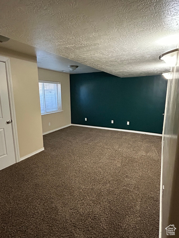 Carpeted empty room featuring a textured ceiling and baseboards