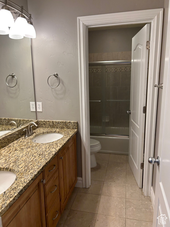Bathroom with toilet, double vanity, tile patterned floors, and enclosed tub / shower combo