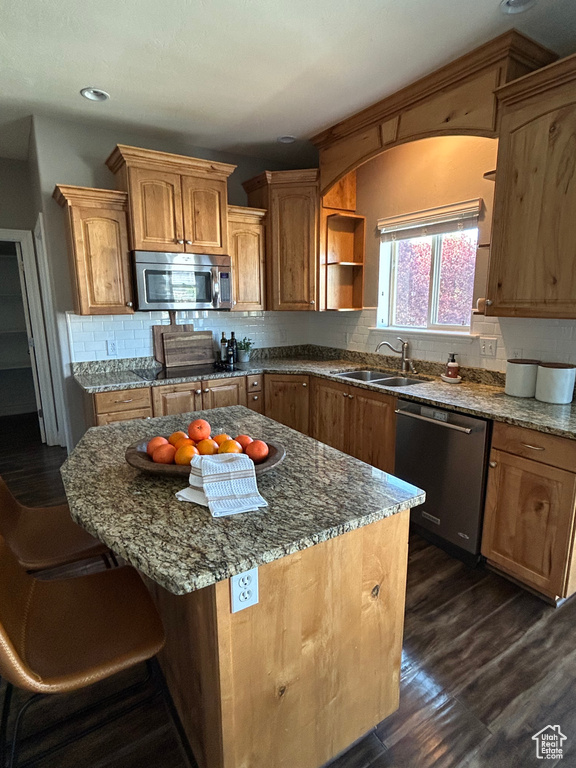 Kitchen featuring appliances with stainless steel finishes, a sink, tasteful backsplash, dark wood-style flooring, and dark stone counters