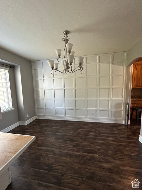 Unfurnished dining area with arched walkways, baseboards, a chandelier, dark wood-type flooring, and a textured ceiling