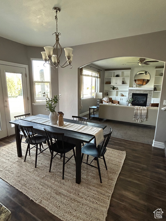 Dining space with arched walkways, dark wood-type flooring, a chandelier, a glass covered fireplace, and baseboards