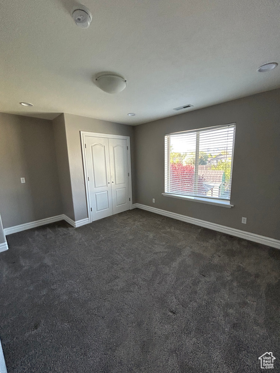 Unfurnished bedroom with baseboards, dark colored carpet, and a closet