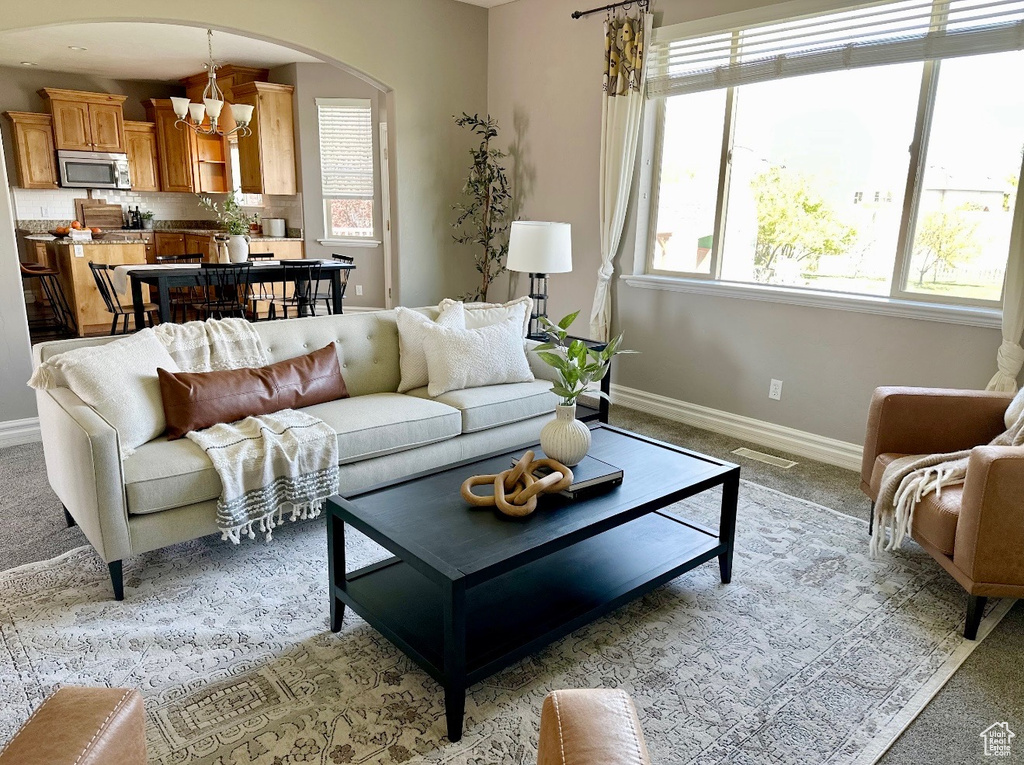 Living area featuring a chandelier, light colored carpet, baseboards, and arched walkways