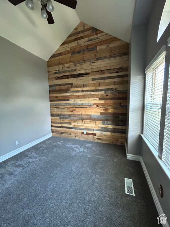 Unfurnished room featuring wooden walls, lofted ceiling, ceiling fan, carpet flooring, and baseboards