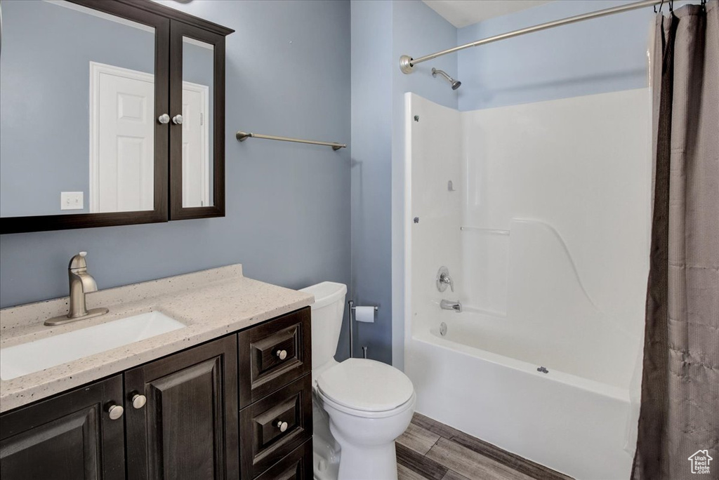 Full bath featuring toilet, vanity, wood finished floors, and shower / bath combination with curtain