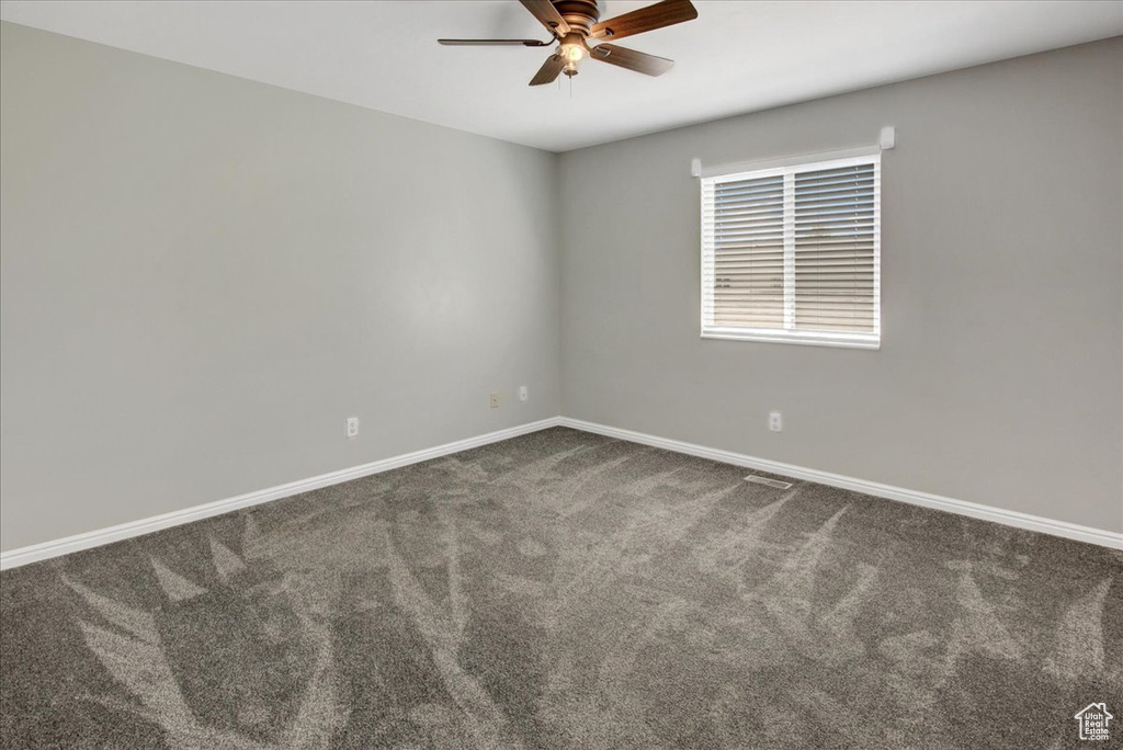 Carpeted empty room featuring a ceiling fan and baseboards