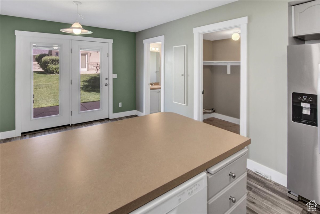 Kitchen featuring stainless steel fridge with ice dispenser, white cabinets, baseboards, wood finished floors, and hanging light fixtures