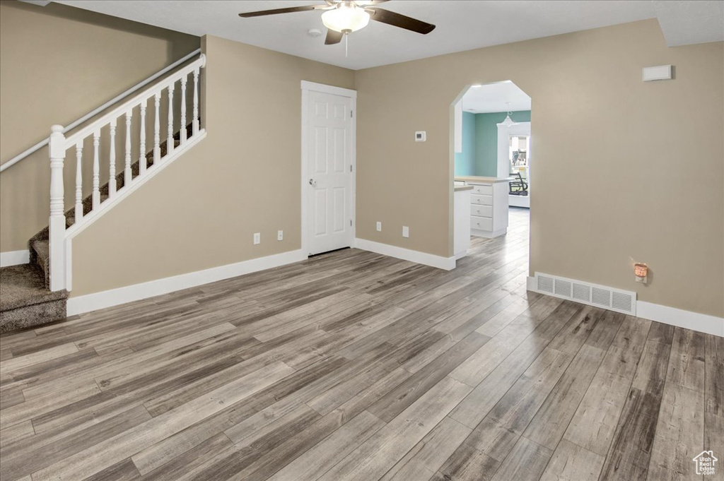 Unfurnished living room featuring ceiling fan, wood finished floors, stairway, and baseboards