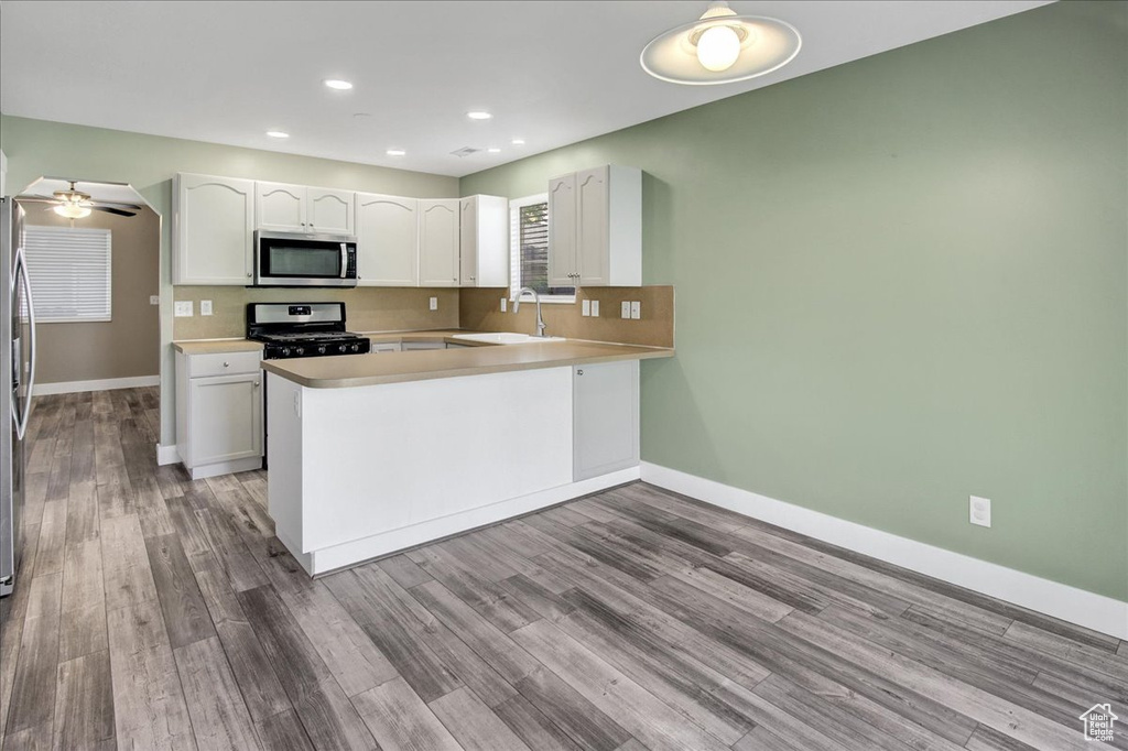 Kitchen with stainless steel appliances, white cabinets, baseboards, a peninsula, and wood finished floors