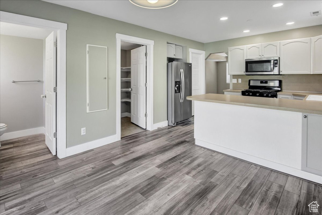 Kitchen with stainless steel appliances, white cabinets, baseboards, wood finished floors, and recessed lighting