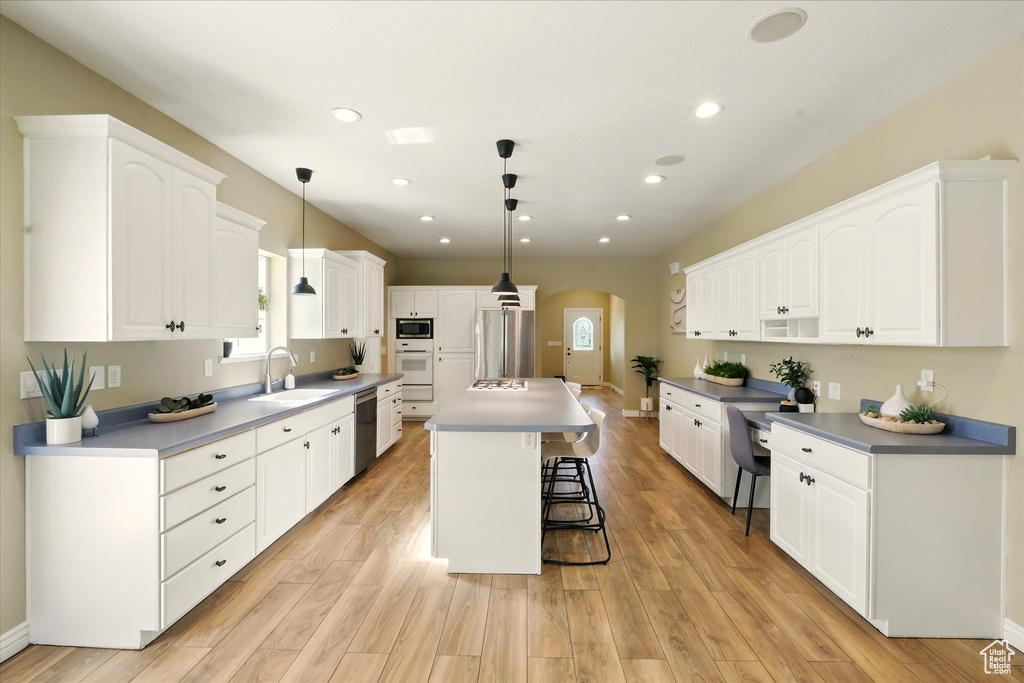 Kitchen featuring arched walkways, appliances with stainless steel finishes, a sink, a kitchen bar, and white cabinets