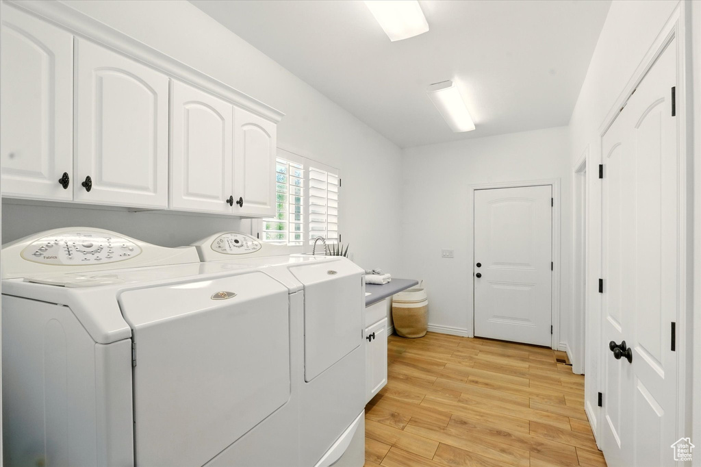 Laundry room with cabinet space, washing machine and clothes dryer, and light wood-style flooring