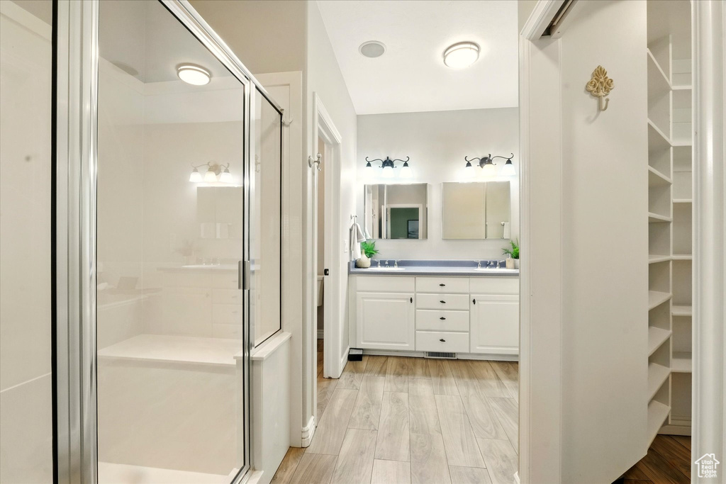 Full bath featuring a shower stall, double vanity, a walk in closet, and wood finished floors
