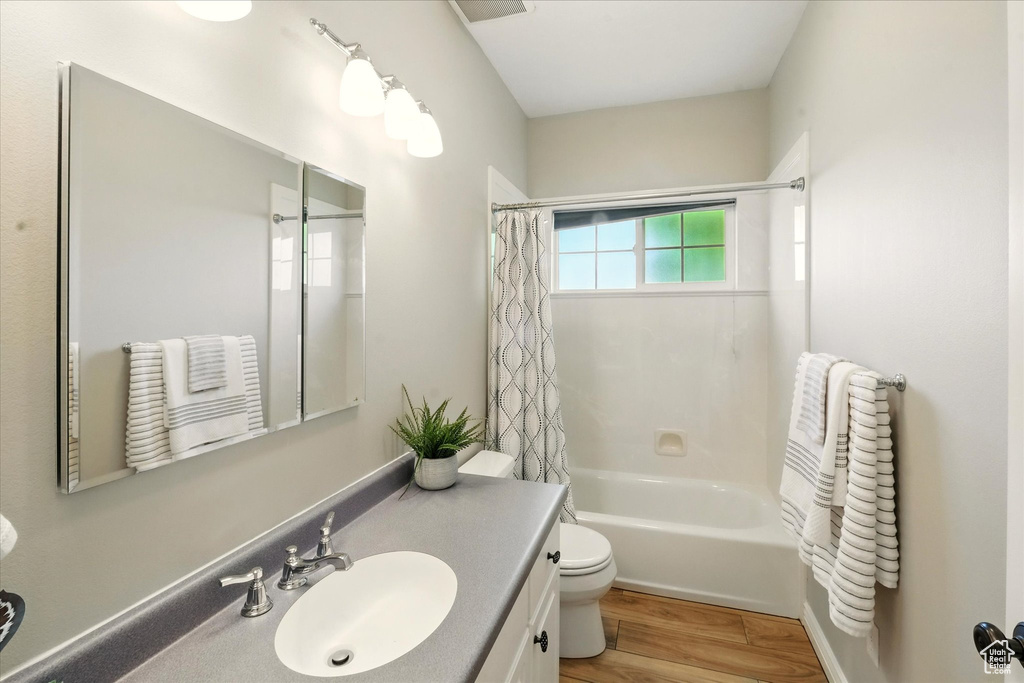 Full bath with vanity, toilet, wood finished floors, and shower / tub combo with curtain