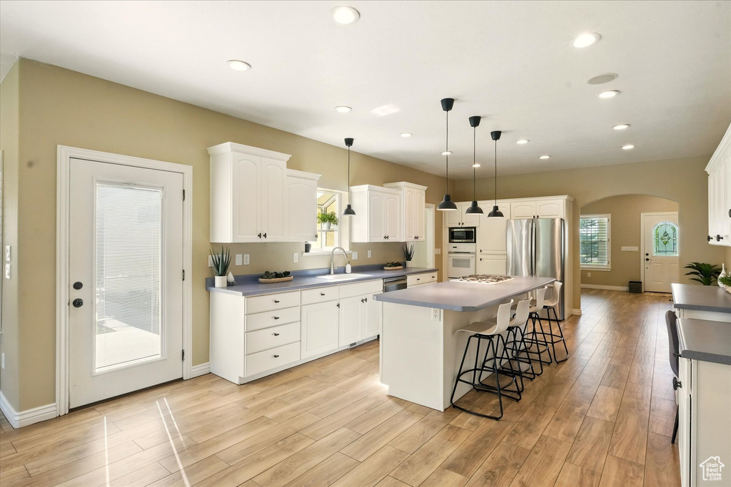 Kitchen with a sink, stainless steel appliances, a kitchen island, arched walkways, and light wood-type flooring