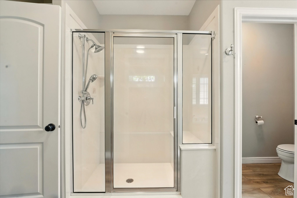 Full bath with a stall shower, wood finished floors, toilet, and baseboards