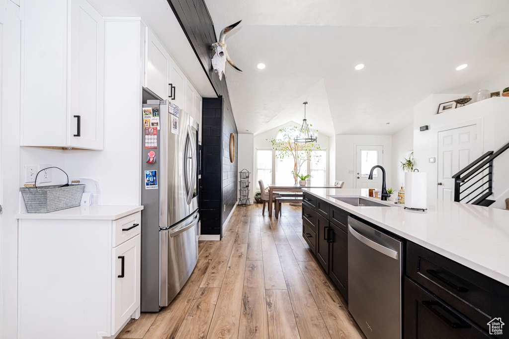 Kitchen featuring a sink, stainless steel appliances, light wood-style floors, white cabinetry, and vaulted ceiling