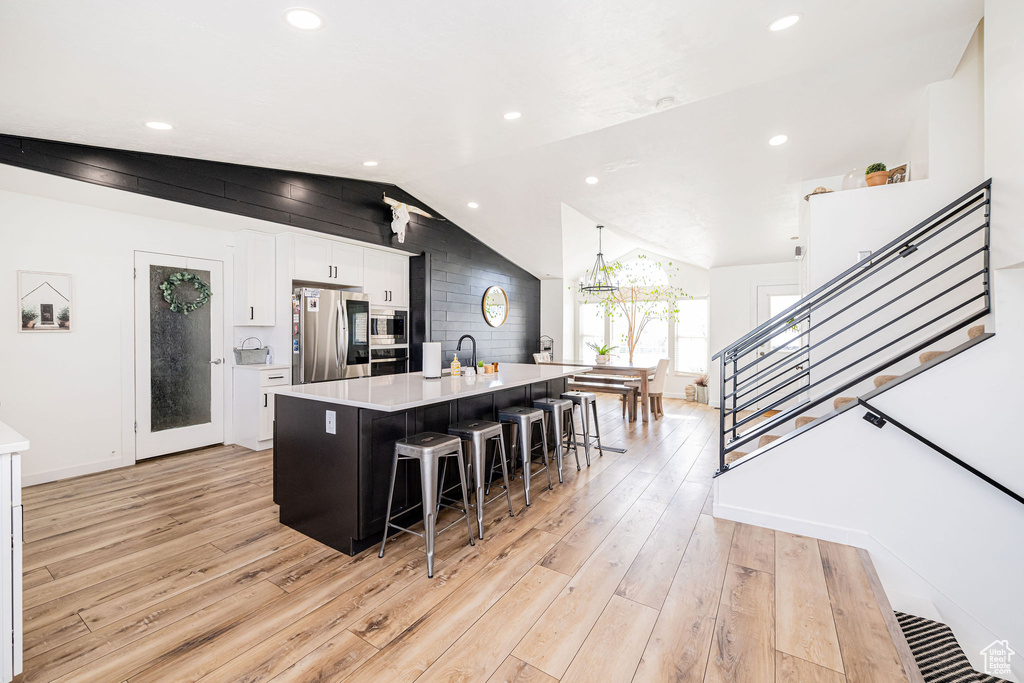 Kitchen with appliances with stainless steel finishes, lofted ceiling, light countertops, light wood-type flooring, and white cabinets