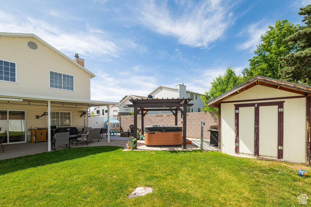 View of yard with a hot tub, a patio area, a storage unit, a pergola, and an outbuilding