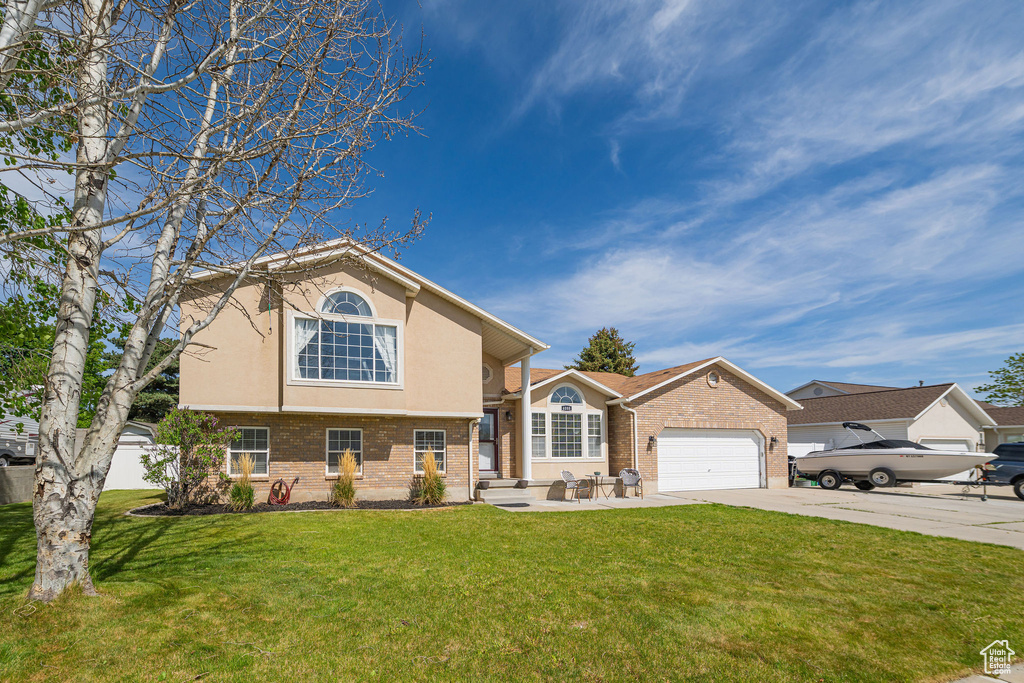 View of front of property featuring brick siding, concrete driveway, a front yard, stucco siding, and an attached garage