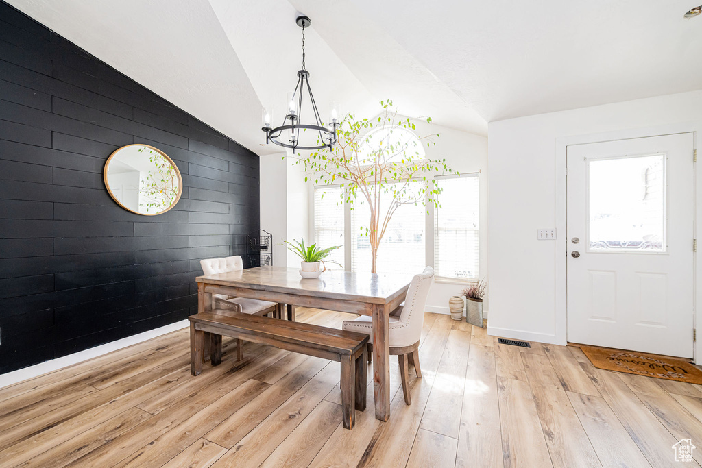 Dining area with a chandelier, light wood-type flooring, vaulted ceiling, baseboards, and an accent wall