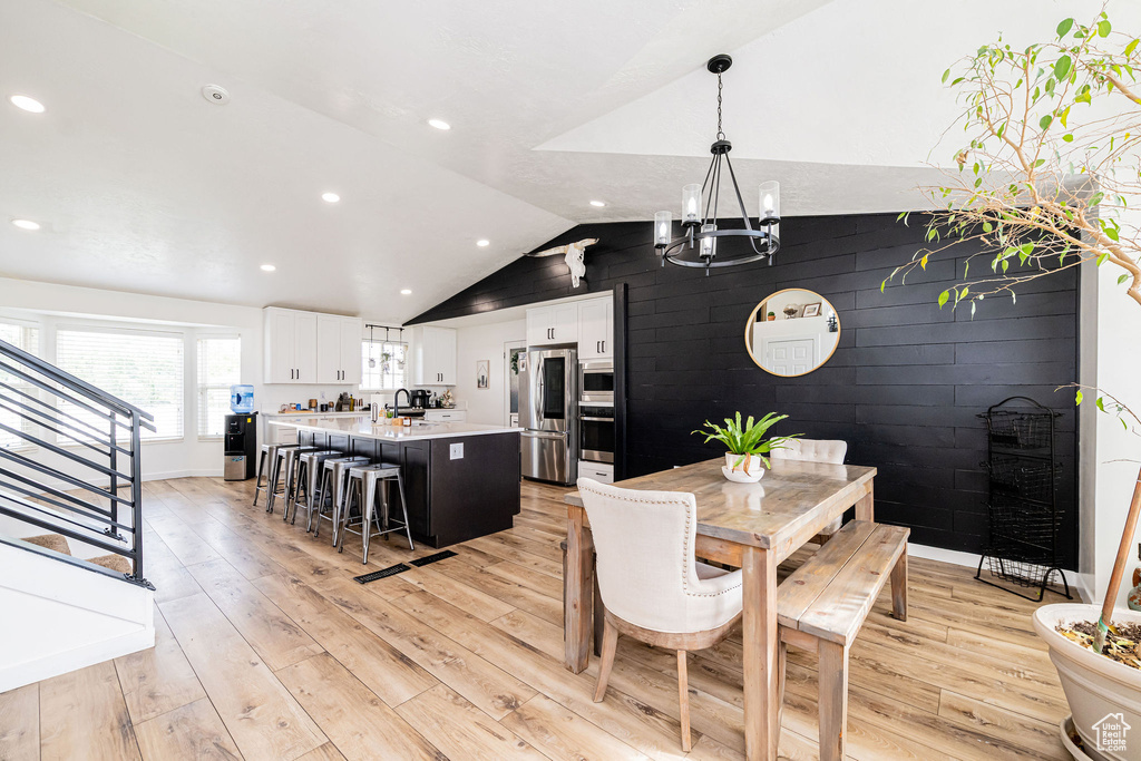 Dining area featuring a chandelier, light wood finished floors, vaulted ceiling, stairs, and baseboards