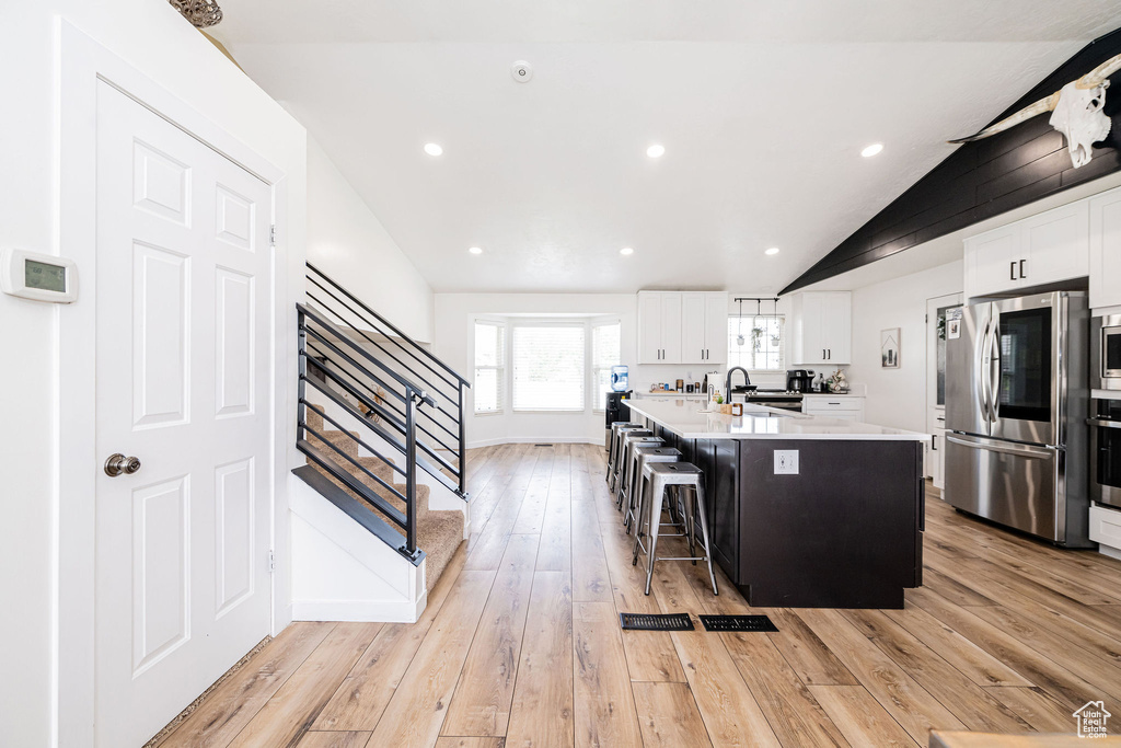 Kitchen with stainless steel appliances, vaulted ceiling, a sink, light countertops, and light wood finished floors