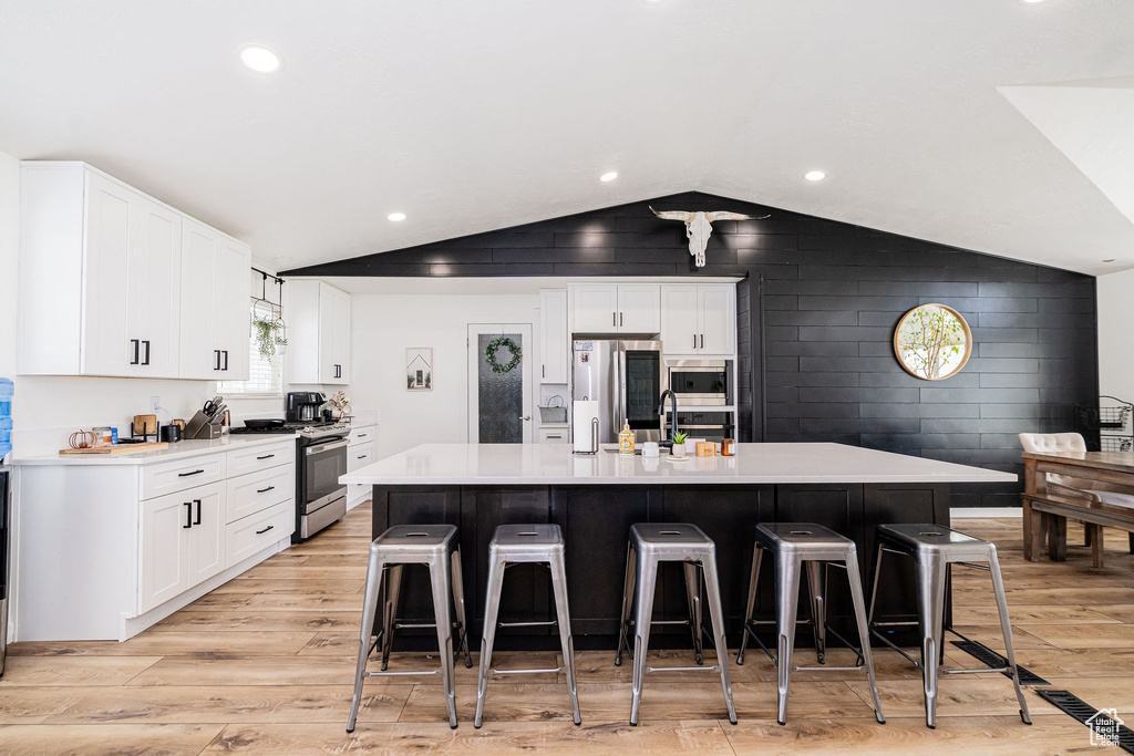 Kitchen with stainless steel appliances, vaulted ceiling, light wood-type flooring, light countertops, and a kitchen breakfast bar