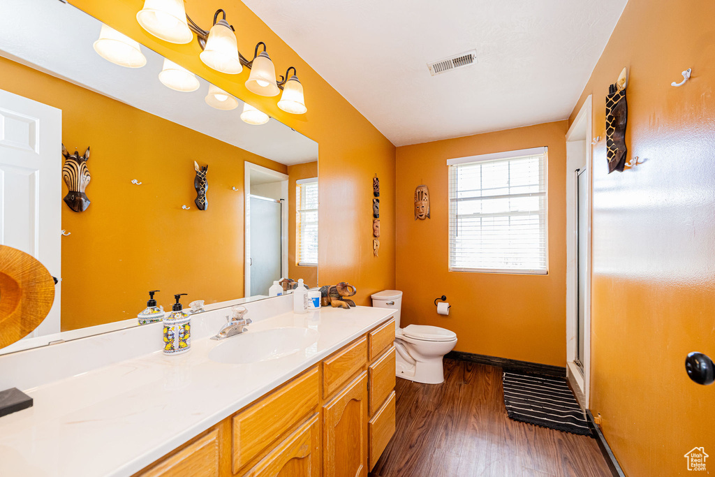 Bathroom featuring a stall shower, toilet, baseboards, wood finished floors, and vanity