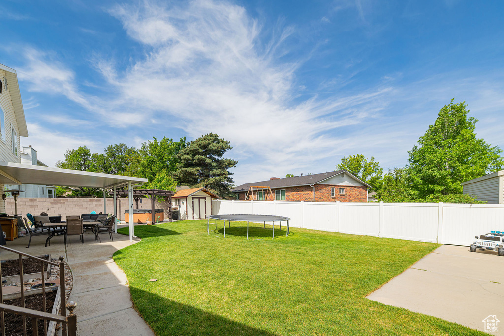 View of yard featuring a patio area, a storage unit, a trampoline, and an outbuilding