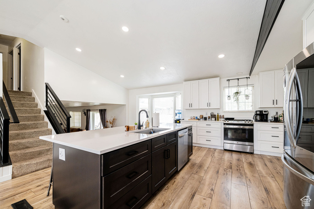 Kitchen featuring stainless steel appliances, a sink, white cabinetry, lofted ceiling, and an island with sink