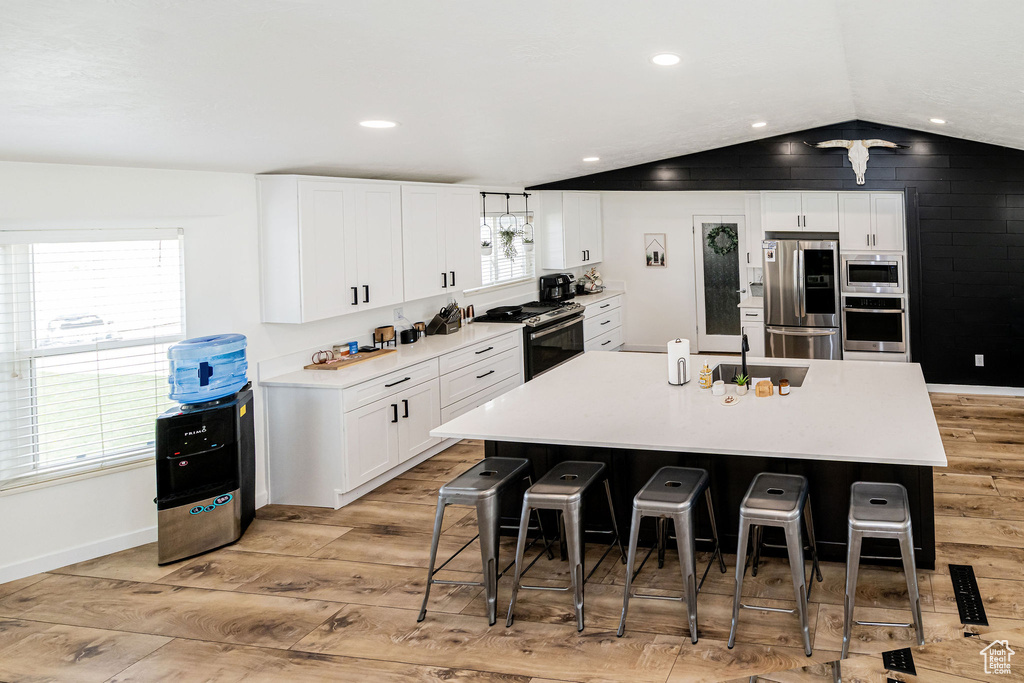 Kitchen featuring appliances with stainless steel finishes, light wood-style floors, a breakfast bar area, a center island with sink, and white cabinets
