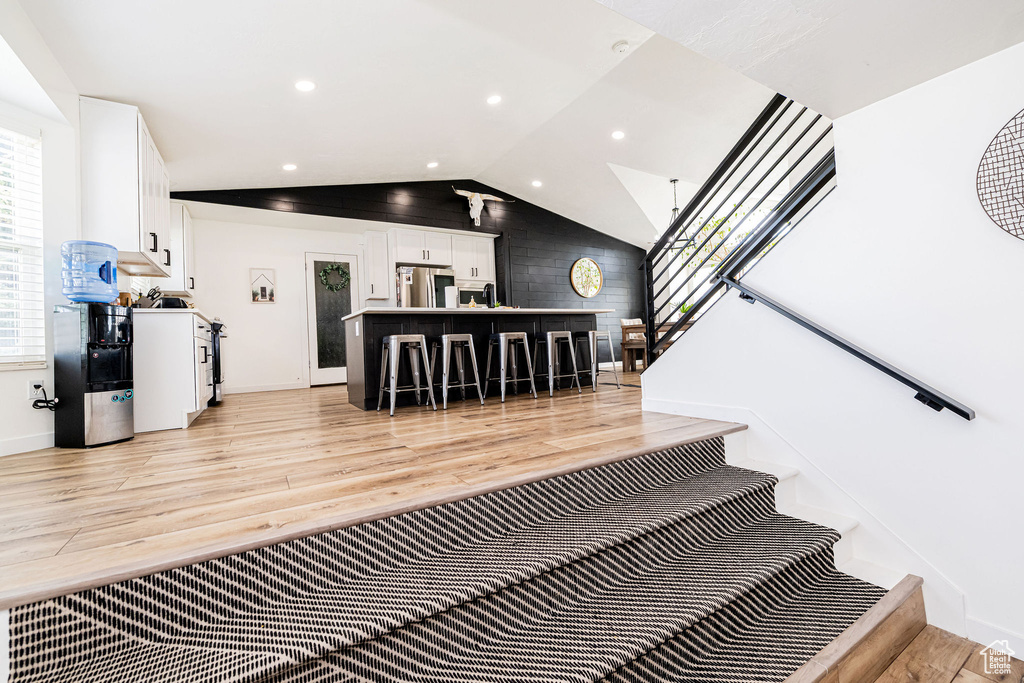 Stairs with wood finished floors, vaulted ceiling, baseboards, and recessed lighting
