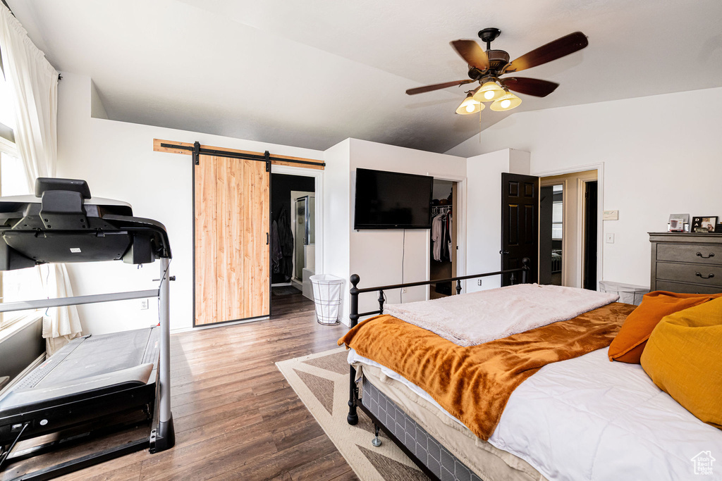 Bedroom with wood finished floors, a barn door, vaulted ceiling, and a ceiling fan