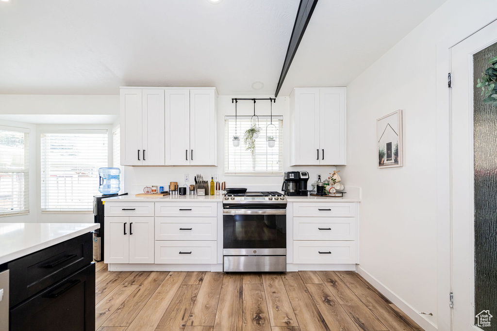 Kitchen featuring stainless steel range with gas stovetop, light countertops, light wood-type flooring, white cabinets, and baseboards