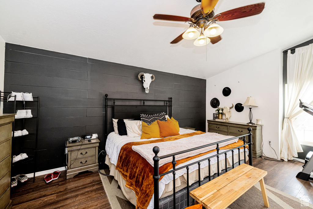 Bedroom with wood finished floors, an accent wall, and ceiling fan